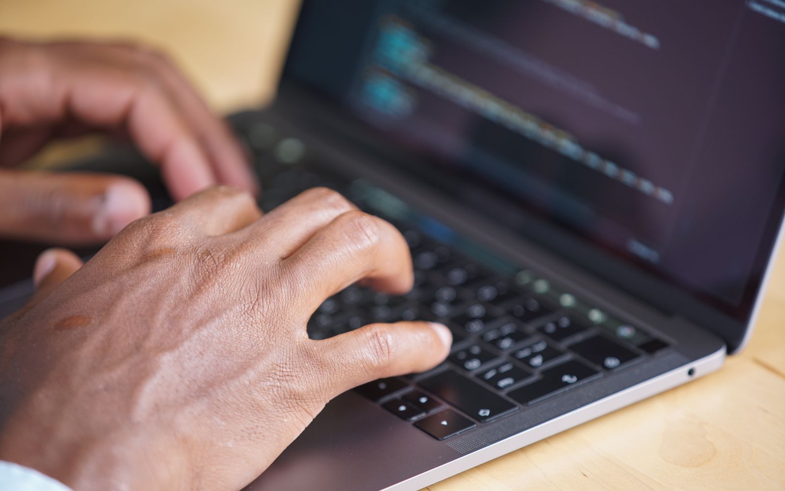 Hands typing on a laptop with code displayed on screen, showcasing technology use.