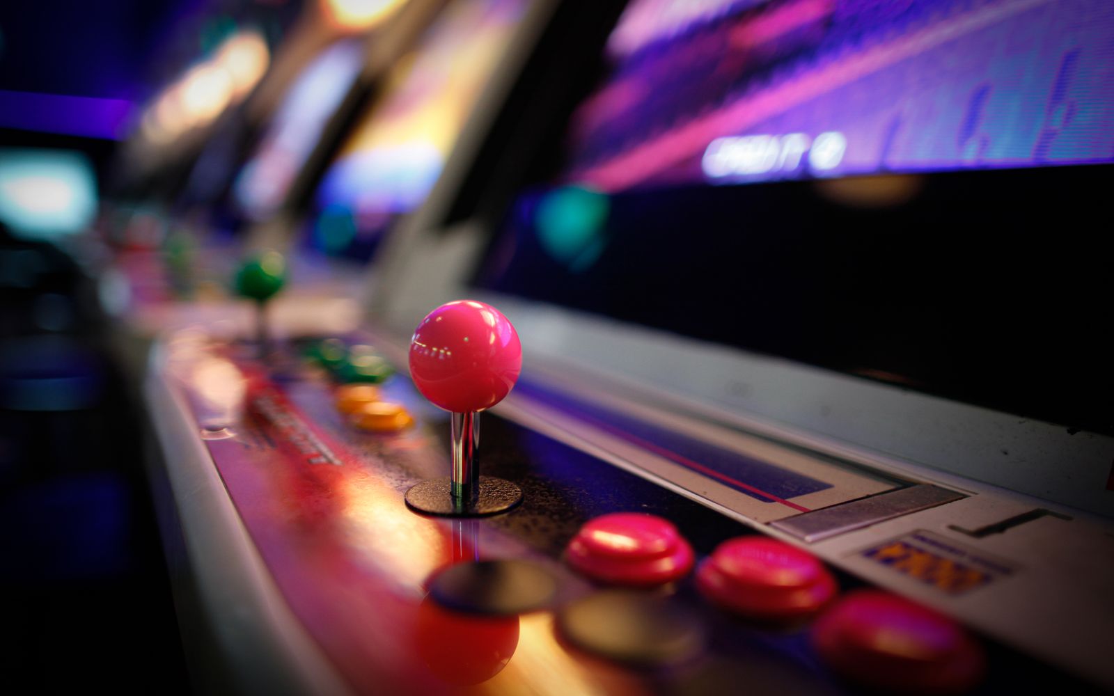 Close-up of a colorful vintage arcade machine with glowing joysticks and buttons in a dimly lit game room.