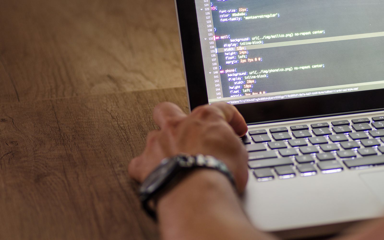 A developer's hand interacting with code on a laptop screen in a workspace setting.