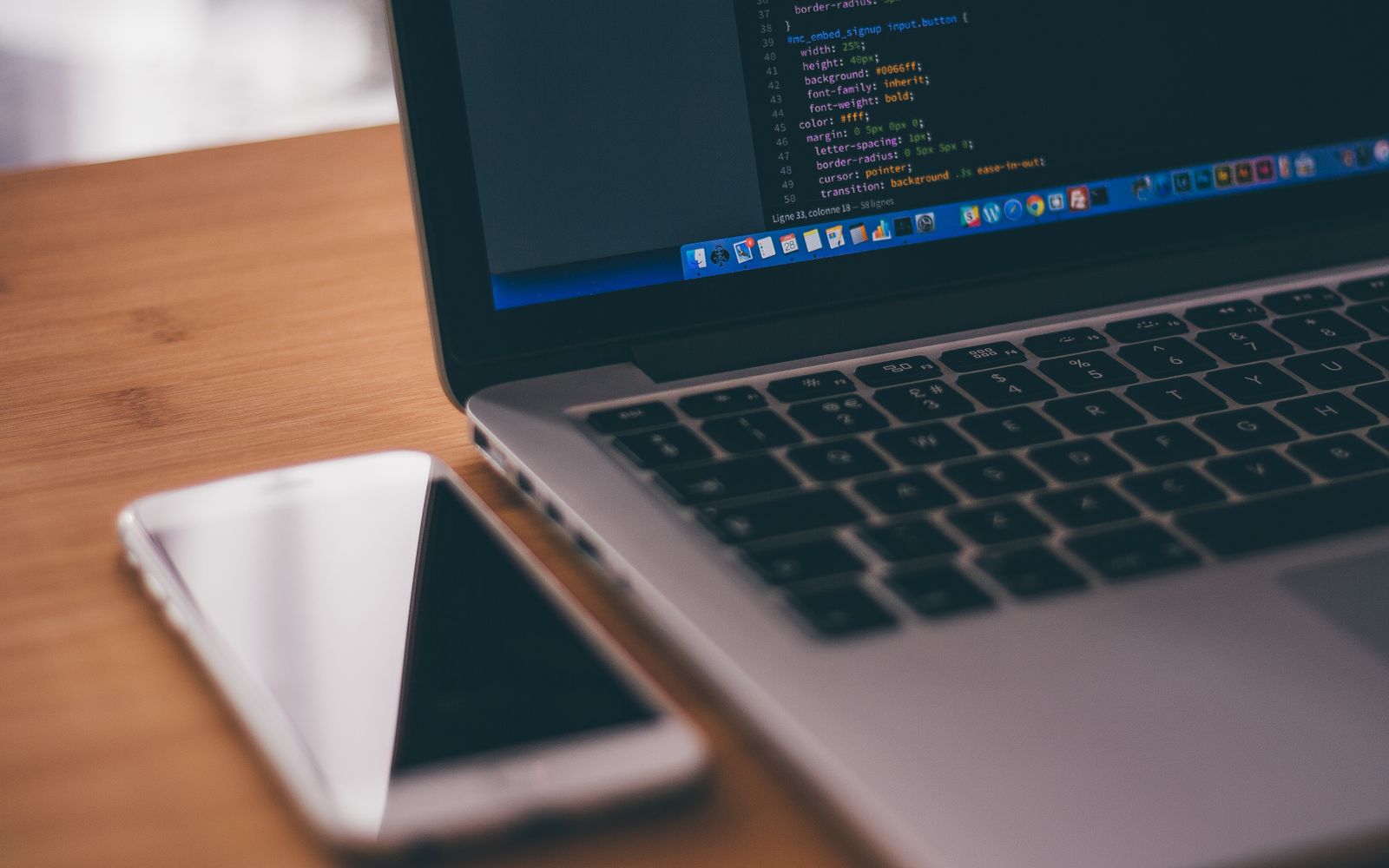 Coding setup with laptop displaying code and smartphone on a wooden table, ideal for tech themes.