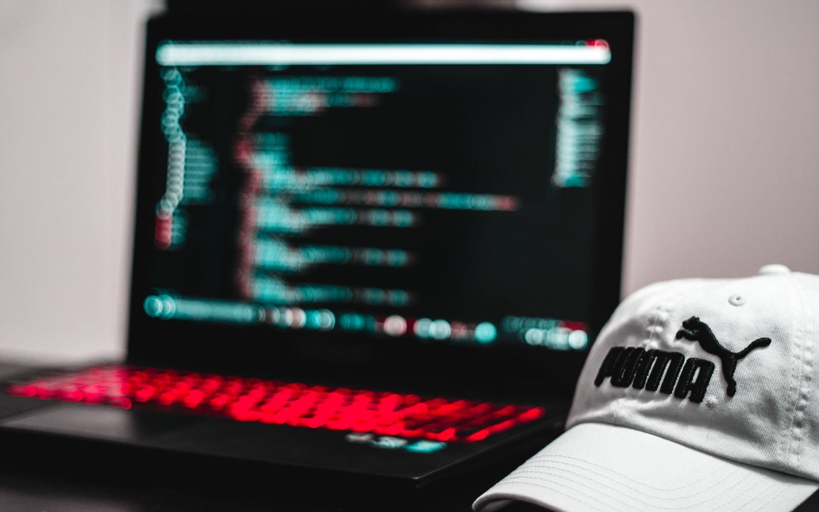Blurred laptop screen displaying code with a white cap in focus, depicting a tech workspace.