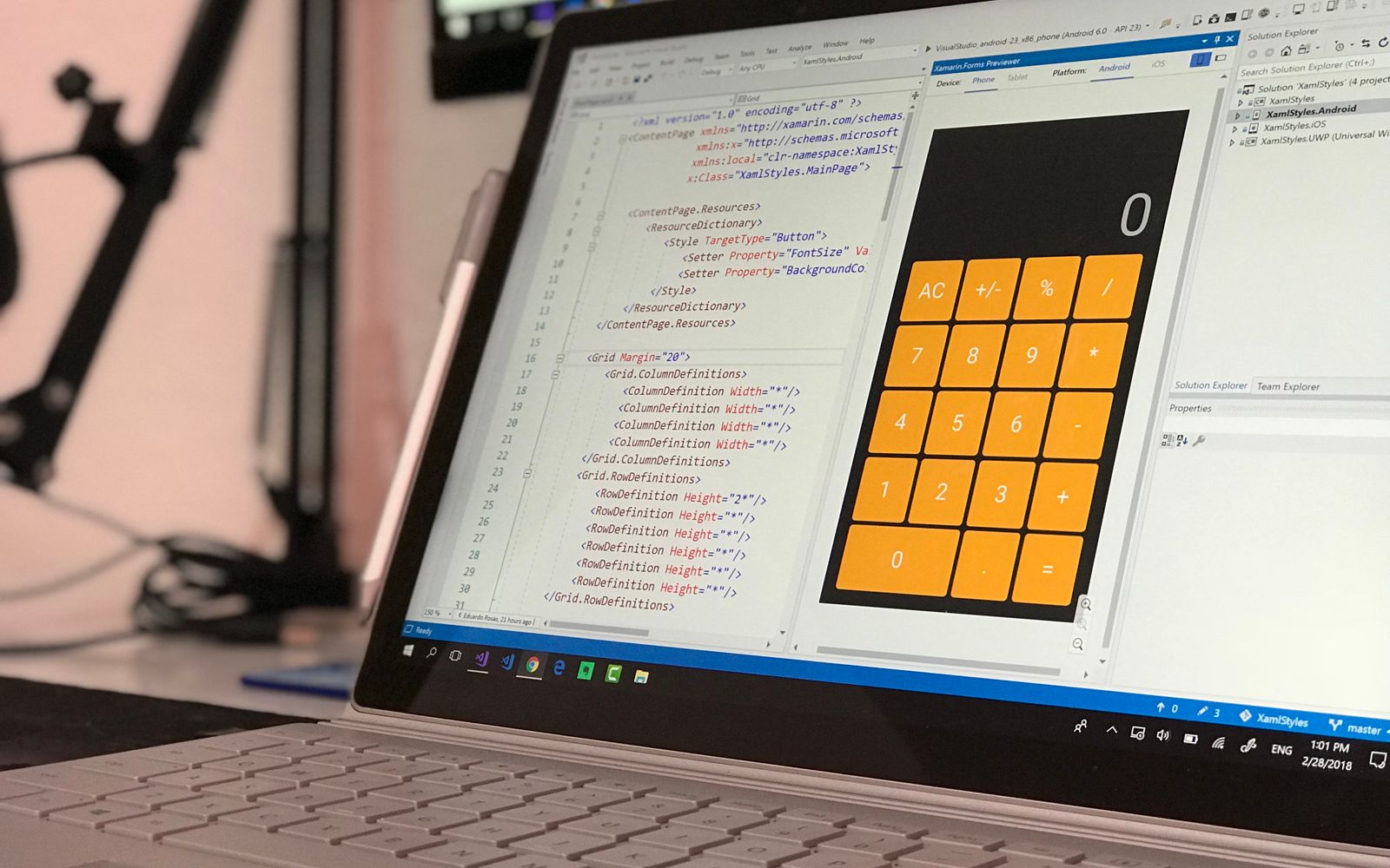 A laptop screen shows a coding application with a calculator design in a tech office setting.