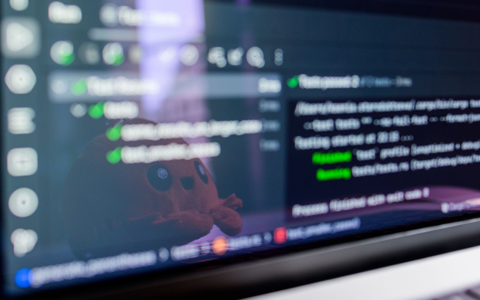 Close-up of a laptop screen displaying programming code with a cute plush toy reflecting.