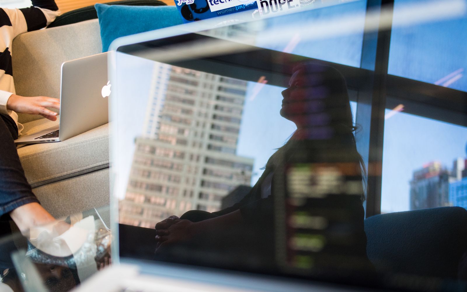 A woman is reflected on a laptop screen displaying code, set in a modern city office scene.