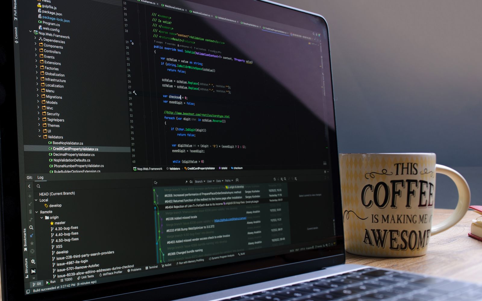 Close-up of laptop with coding software and a motivational coffee mug on a desk.