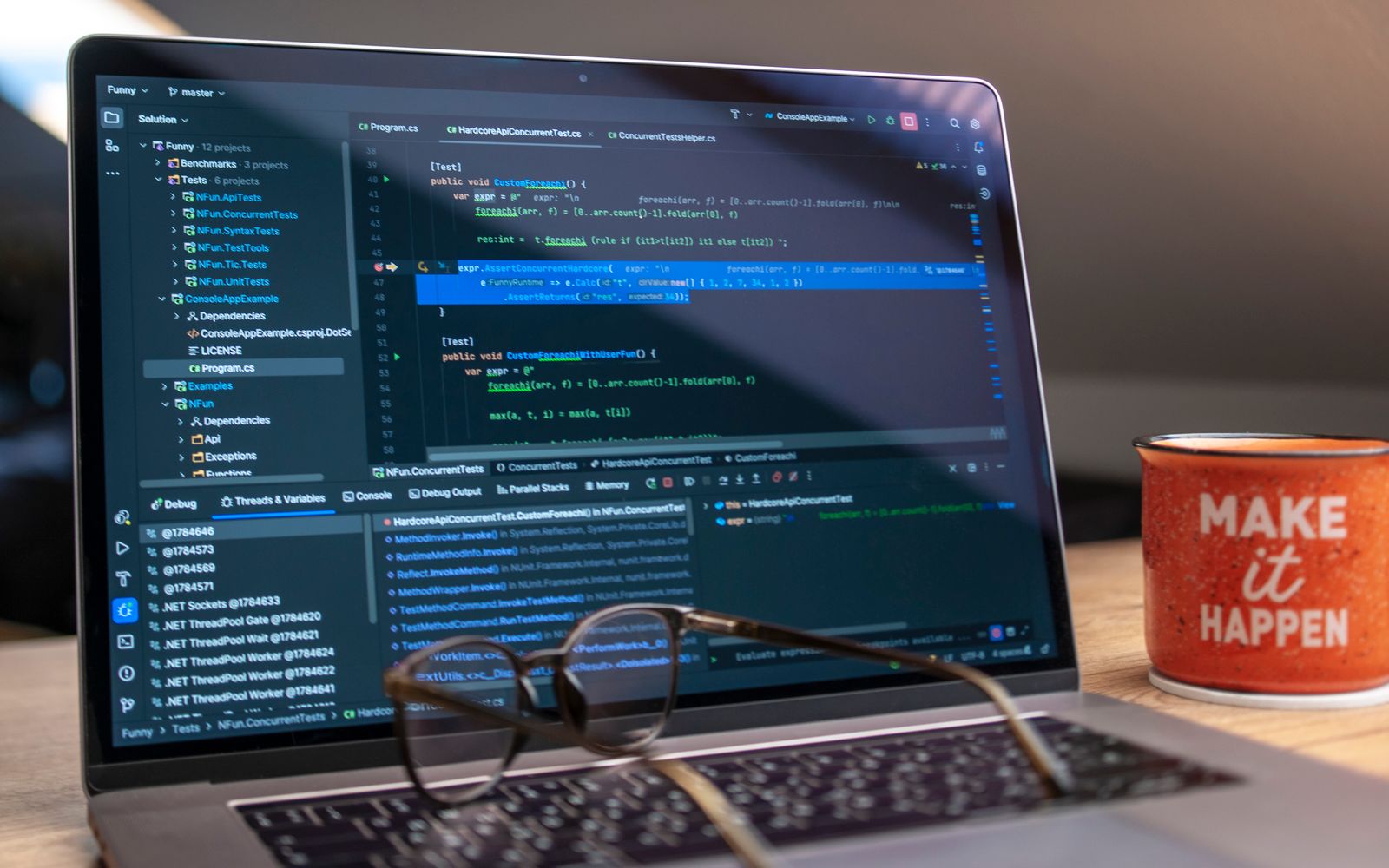 A laptop displaying code editor with a motivational mug that reads 'Make It Happen' on a workspace.
