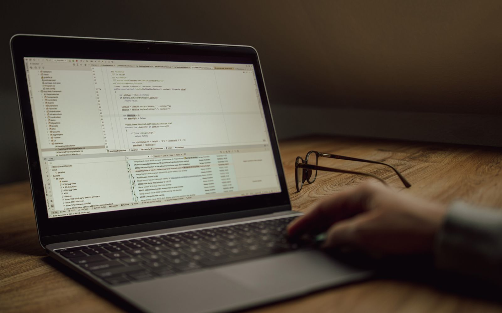 Person working on programming code on a laptop indoors. Glasses on the table.