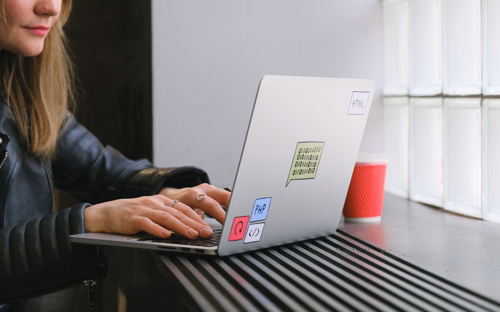 Woman using a laptop by a window in a cafe with a coffee. Ideal for tech and lifestyle themes.