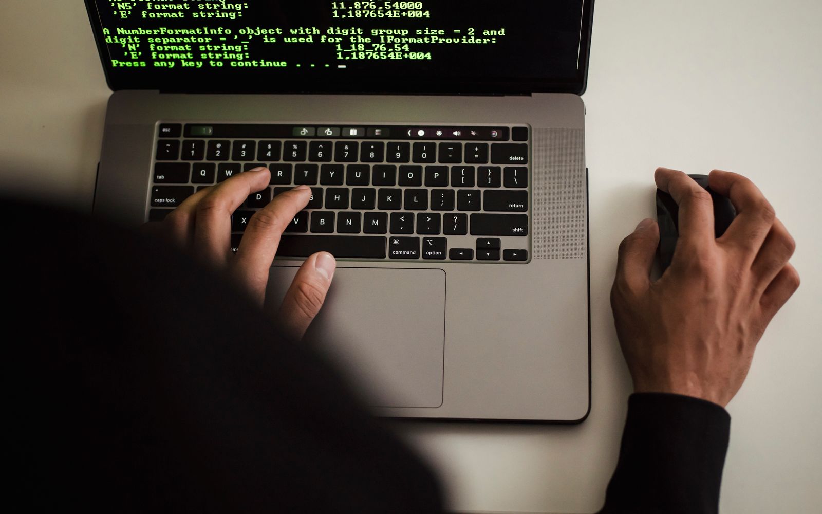 From above crop unrecognizable male developer in black hood working on software code on modern netbook in office