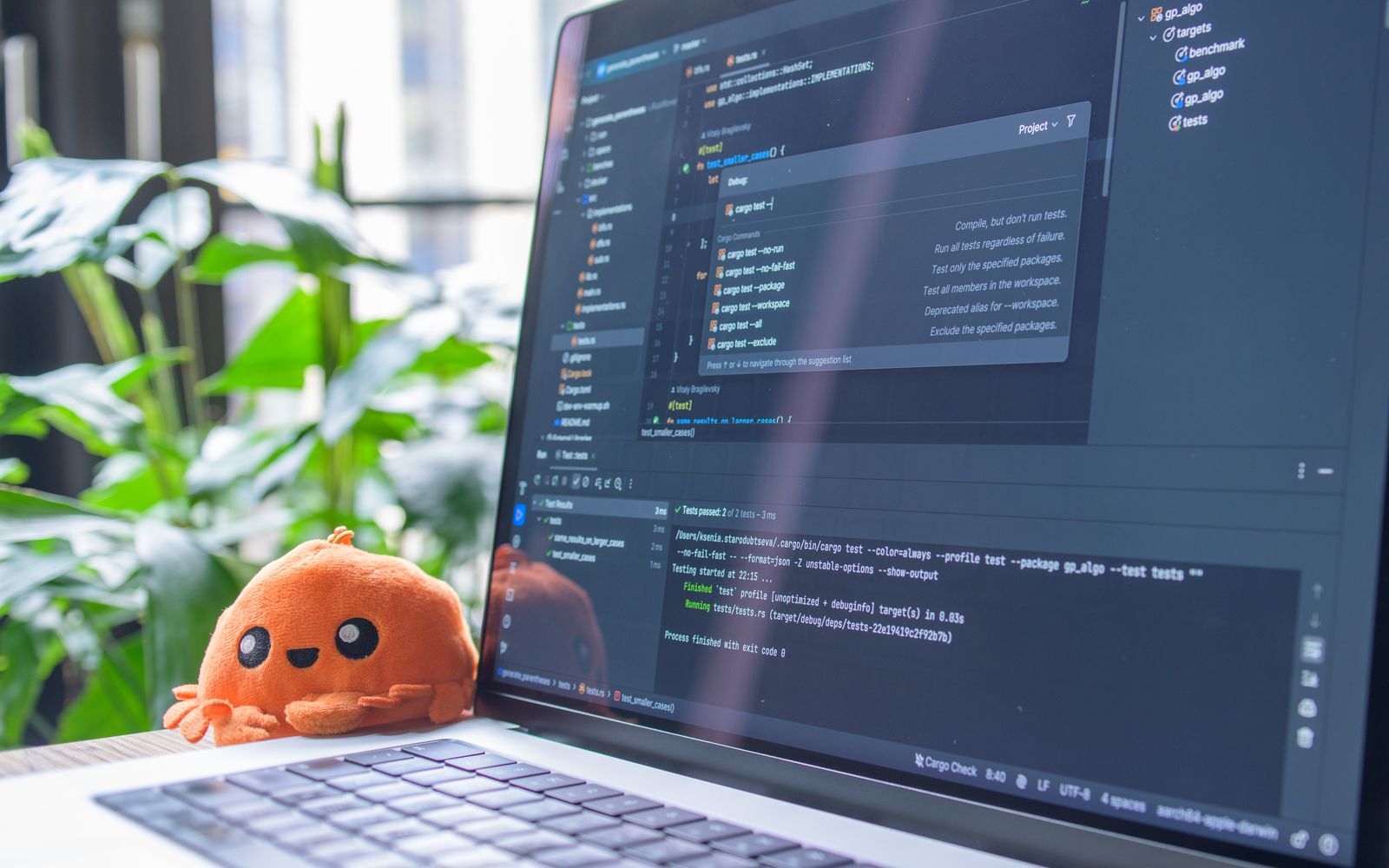 Open laptop with code editor displaying, next to an orange plush toy and green plants.