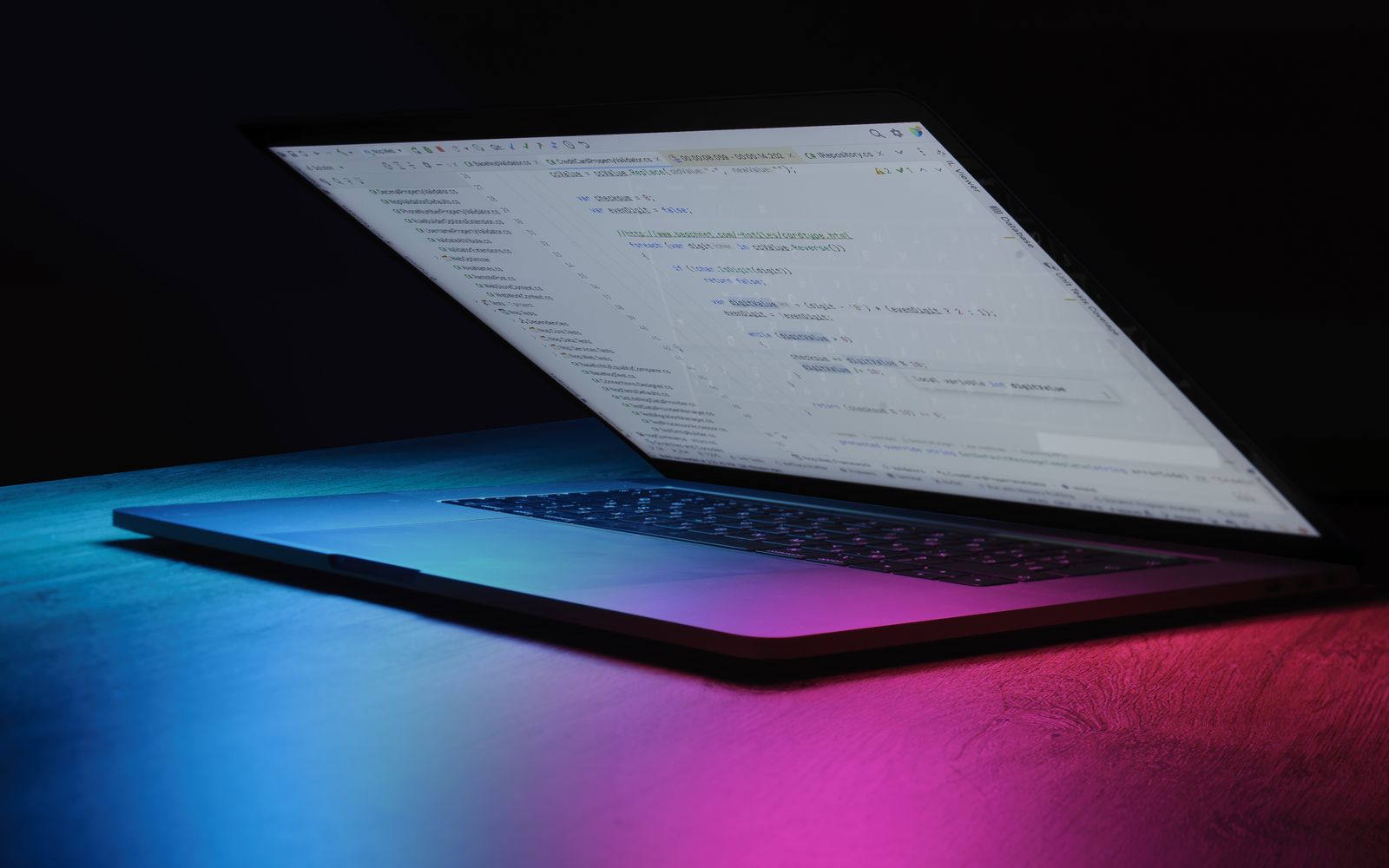 A partially open laptop displaying code, bathed in vibrant neon lighting.