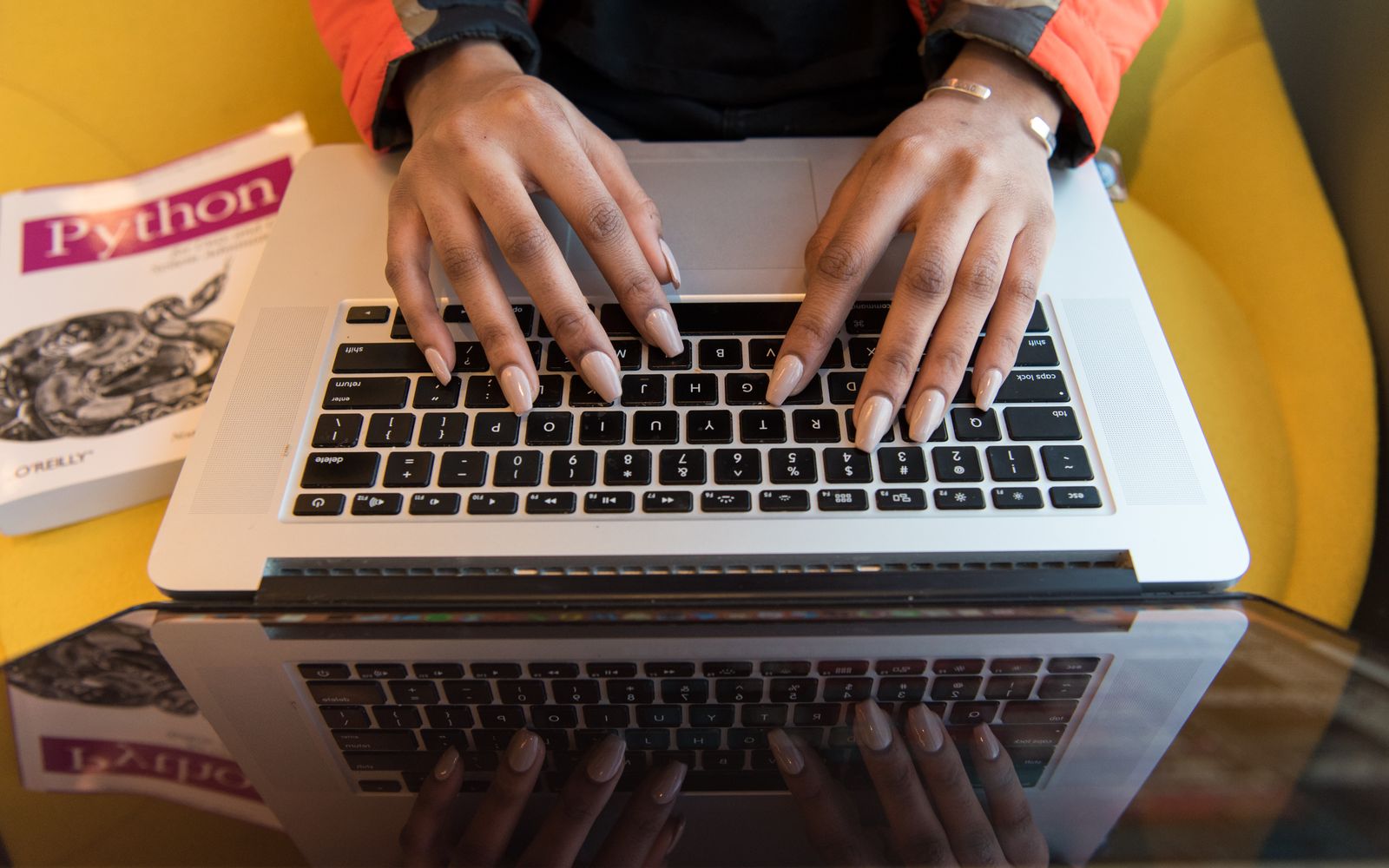 A person typing on a laptop with a Python programming book visible, capturing technology and learning.