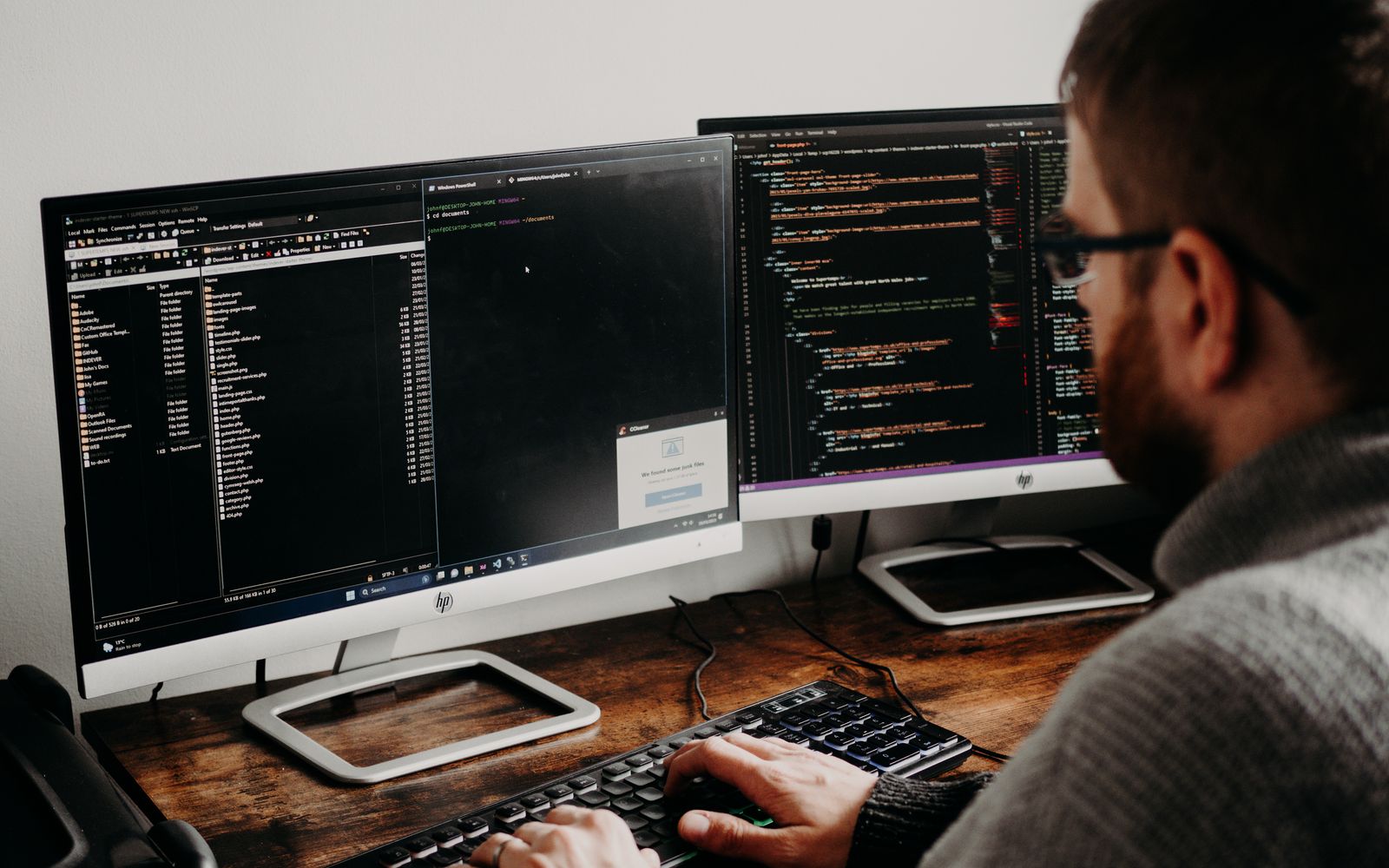 Software developer typing code on dual monitors at a wooden desk.
