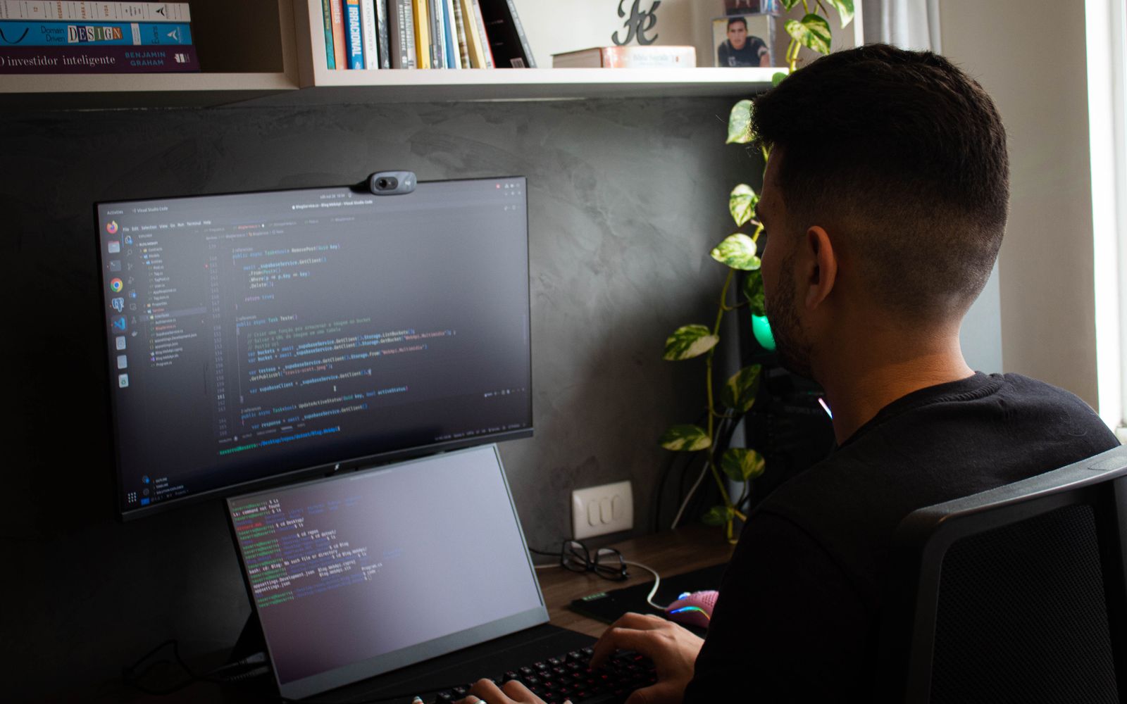 A programmer coding on a laptop and monitor in a stylish office setup.