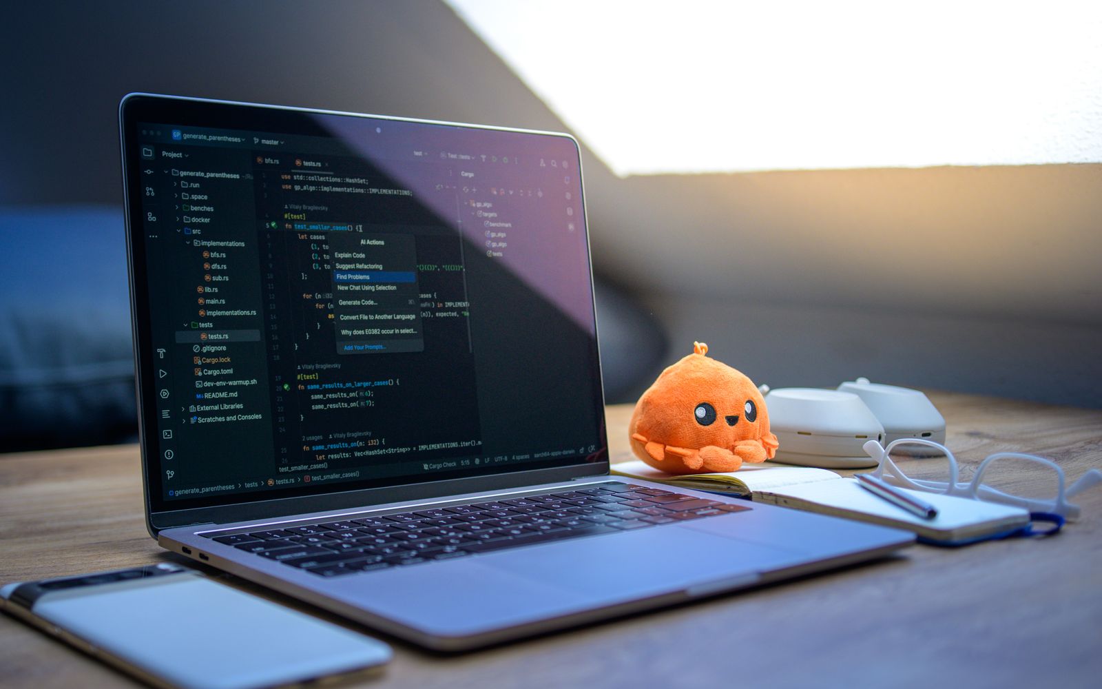 A cozy workspace featuring a laptop displaying code, a smartphone, and a cute orange plush toy on the desk.