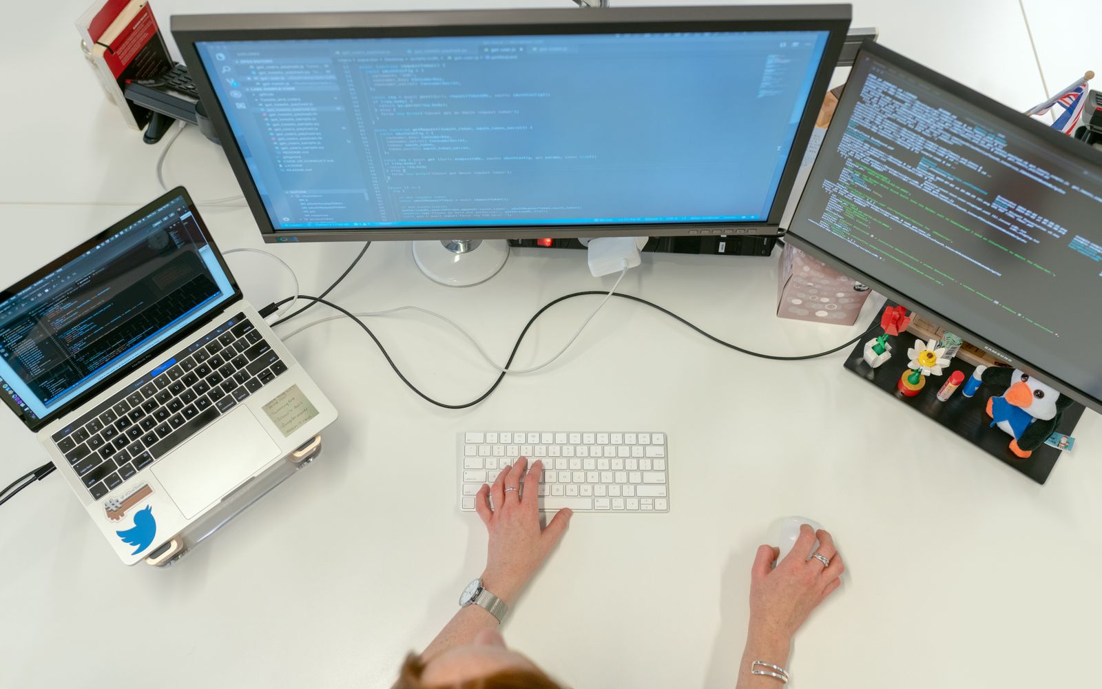 A female software engineer coding on dual monitors and a laptop in an office setting.