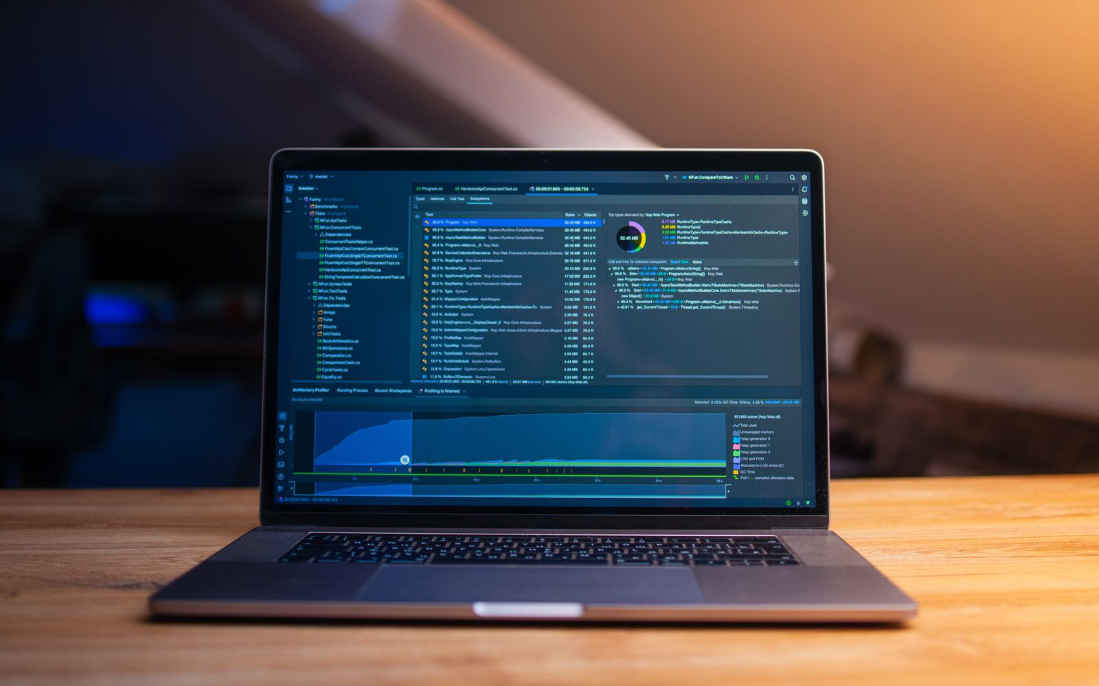 A laptop displaying code on a wooden desk, in a dimly lit workspace.