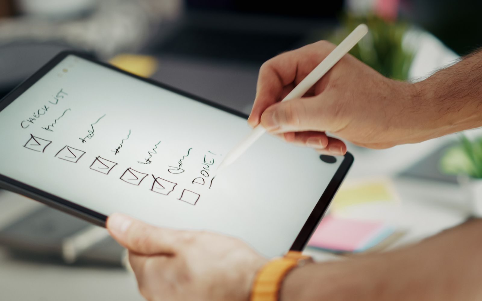 Close-up of a hand writing on a digital checklist using a stylus on a tablet, enhancing productivity.