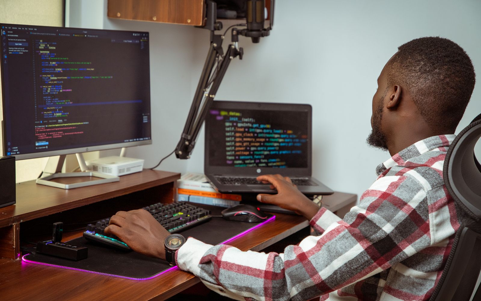 An African man coding on a desktop and laptop in a Nairobi office setting, showcasing modern technology.