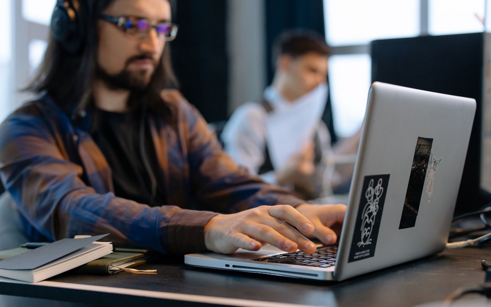A man wearing headphones focused on typing at his laptop in a contemporary office setting.