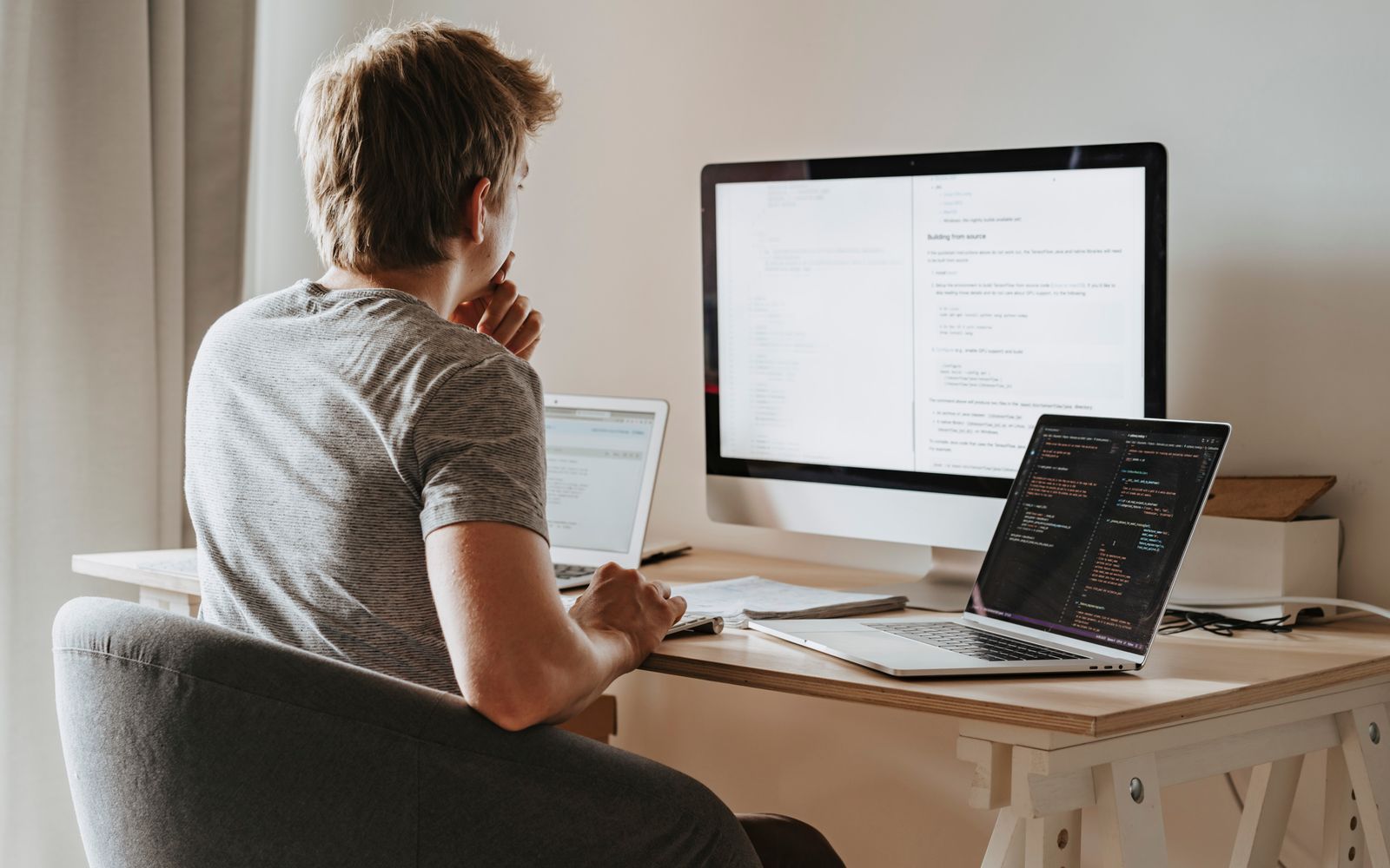 A man deeply engaged in software development with two laptops and a desktop monitor.