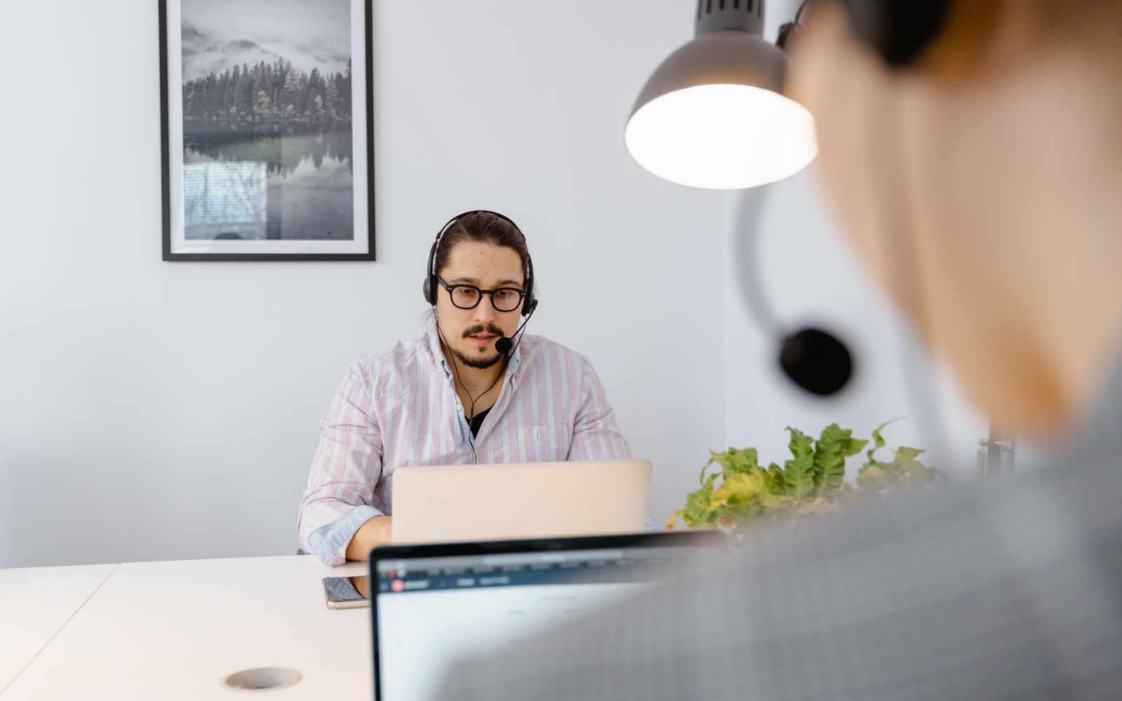 Office scene with a customer support agent wearing headphones, focused on a laptop in a modern workspace.