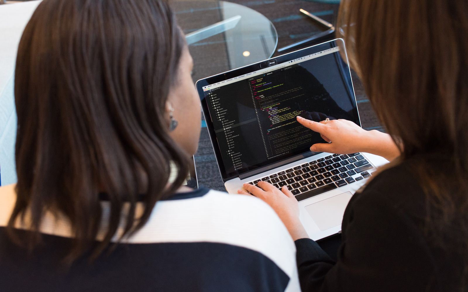 Two women working together on software programming indoors, focusing on code.