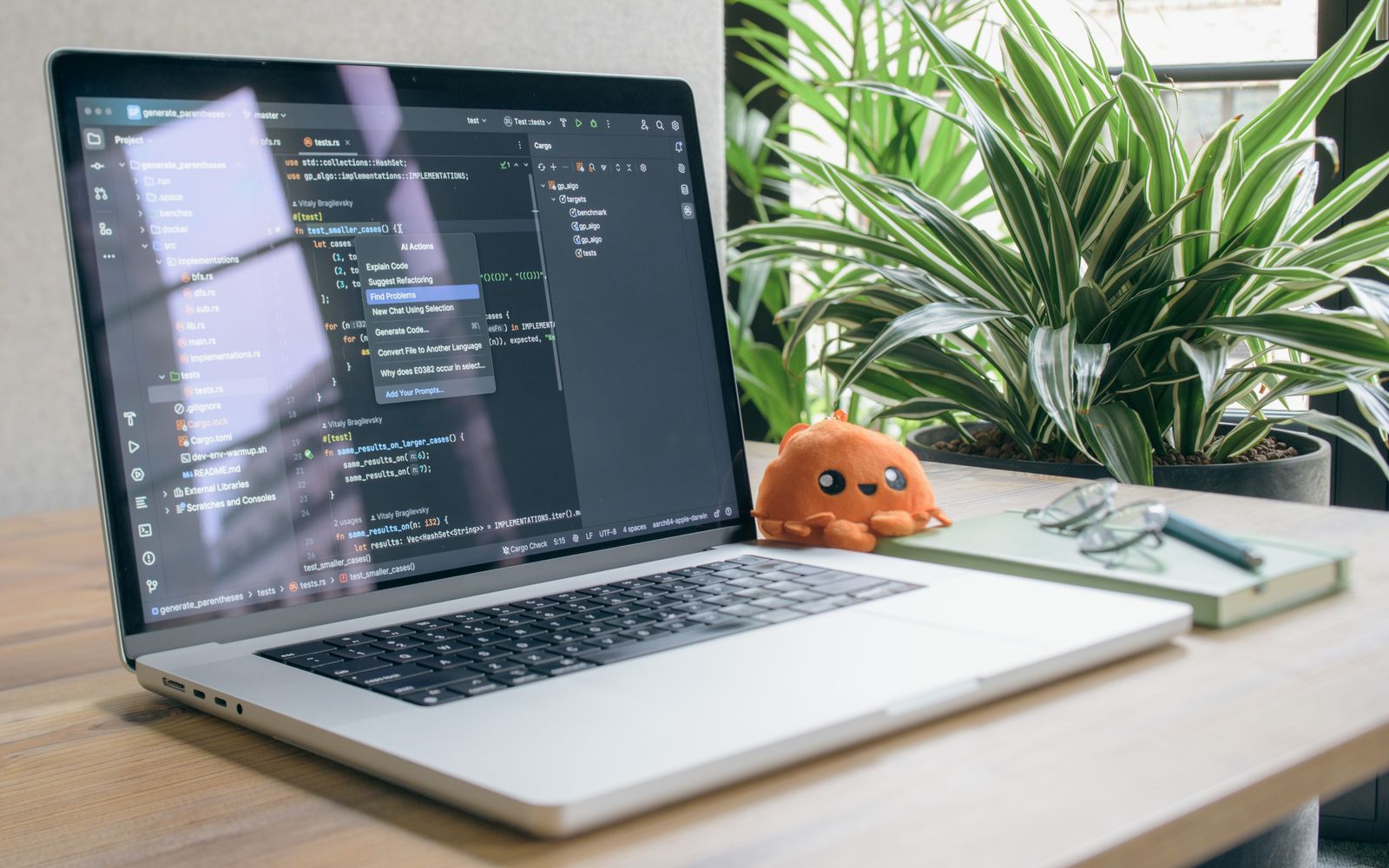 A modern home office setup featuring a laptop with coding software, a plant, and a plush toy.