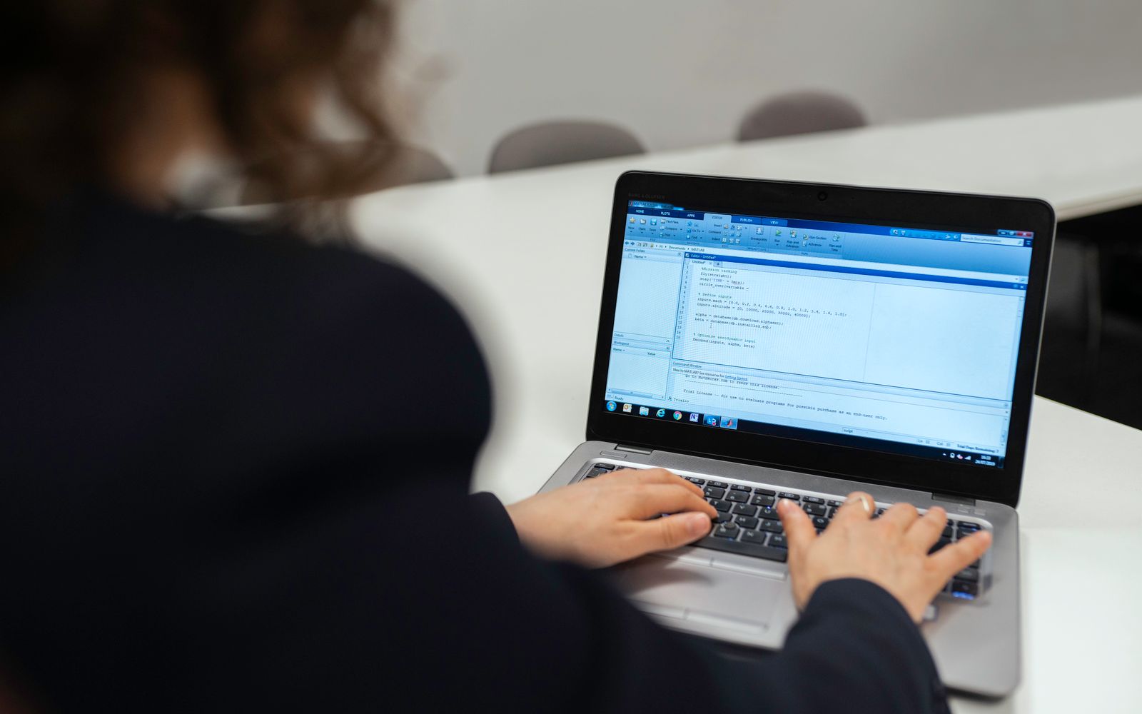 Focused woman coding on a laptop in a modern office setting.