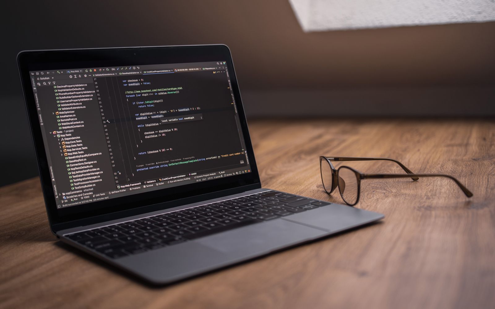 A laptop displaying code editor on a desk next to eyeglasses, ideal for tech themes.