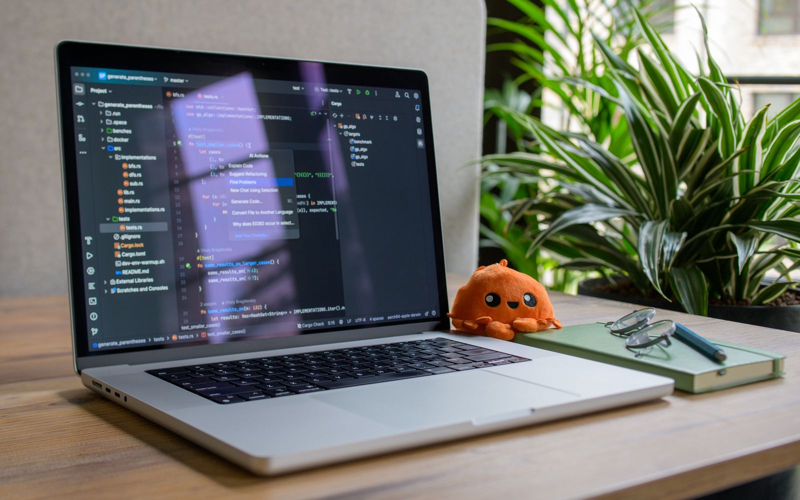 Laptop with coding interface, plant, and toy for a cozy workspace vibe.