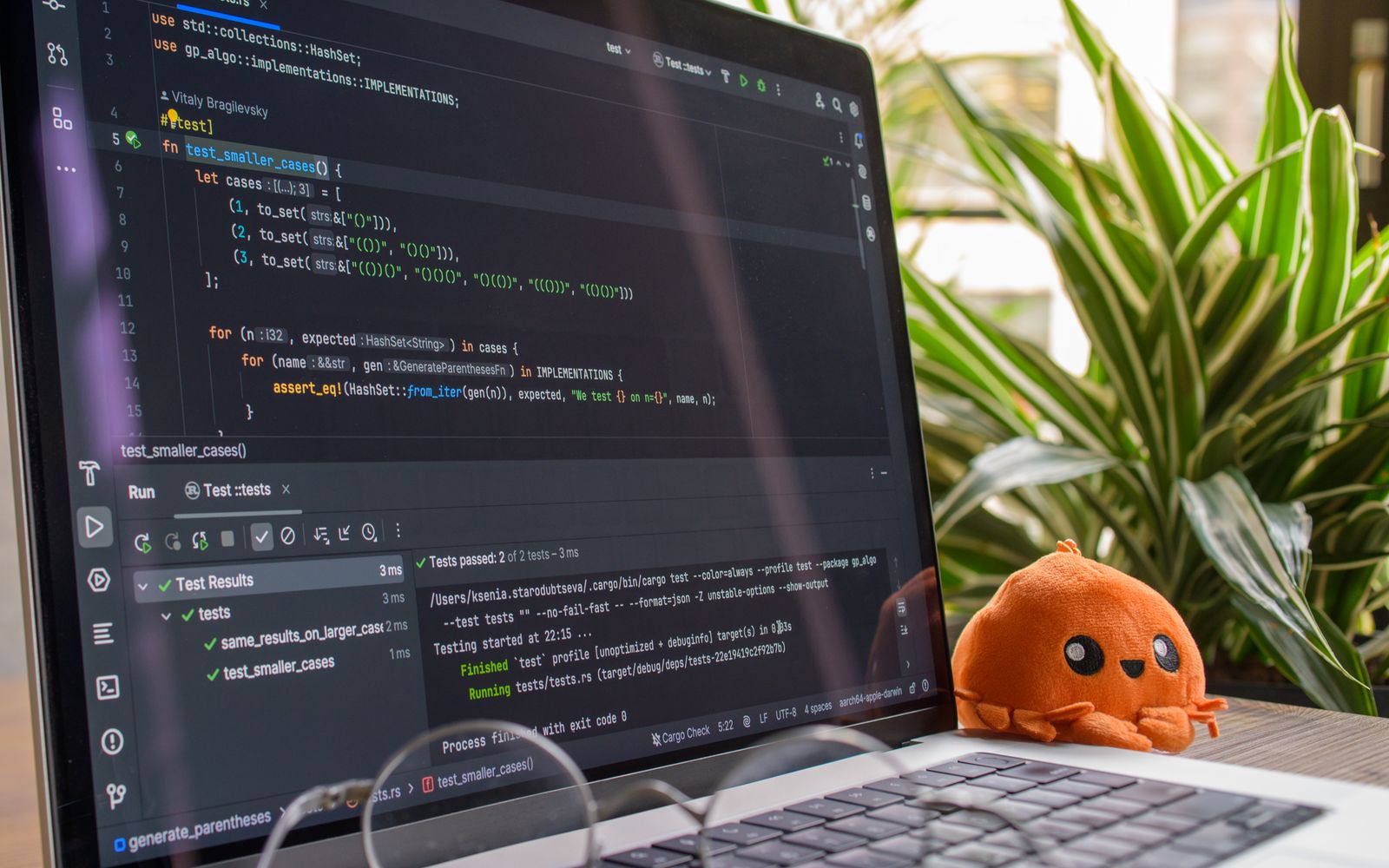 A laptop displaying code in a modern indoor setting with an orange plush toy nearby.