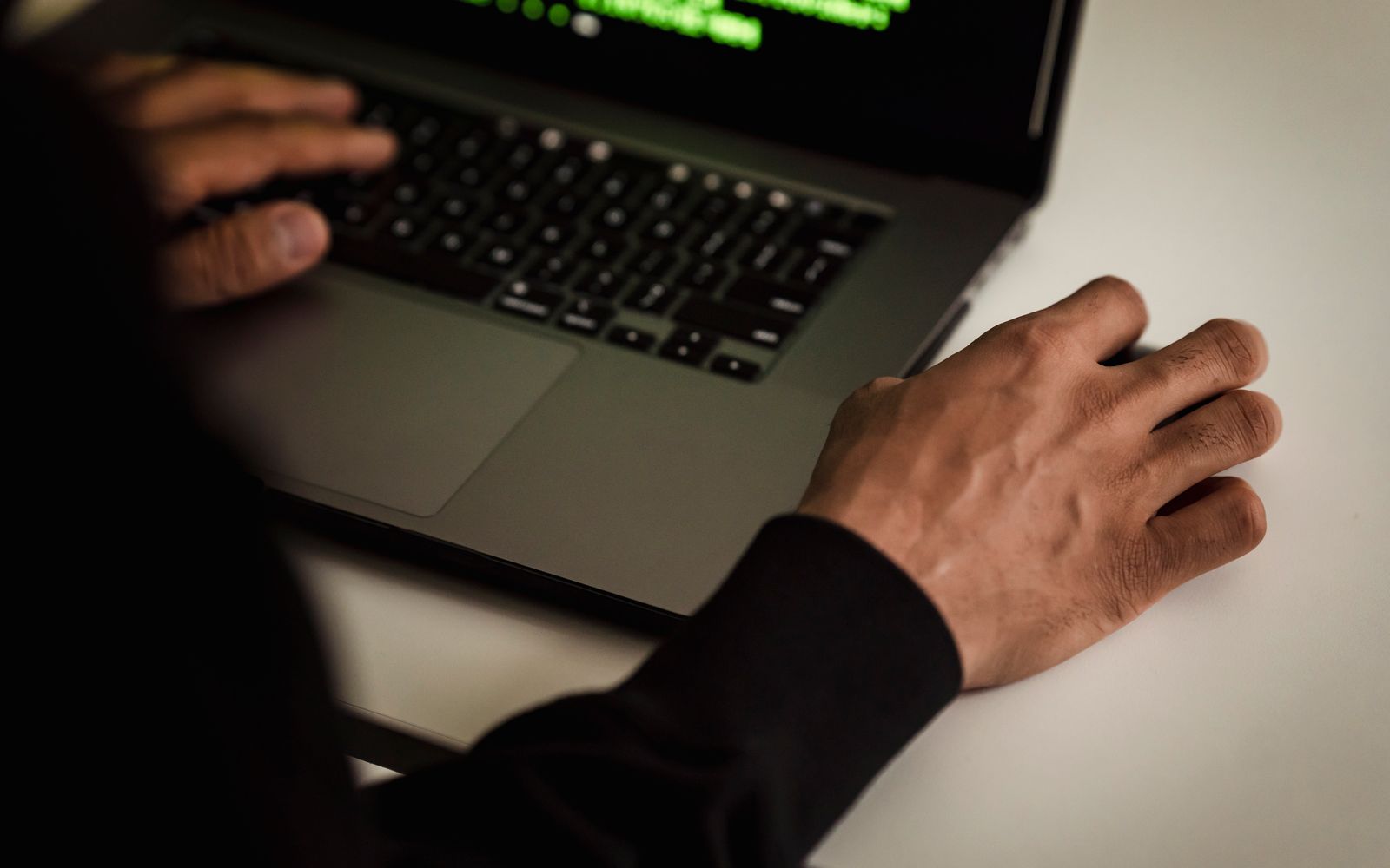 From above crop faceless male developer in black hoodie writing software code on netbook while working in light studio