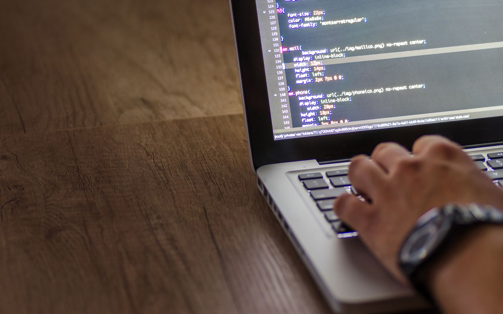 A person is typing code on a laptop, focusing on the screen with programming script.