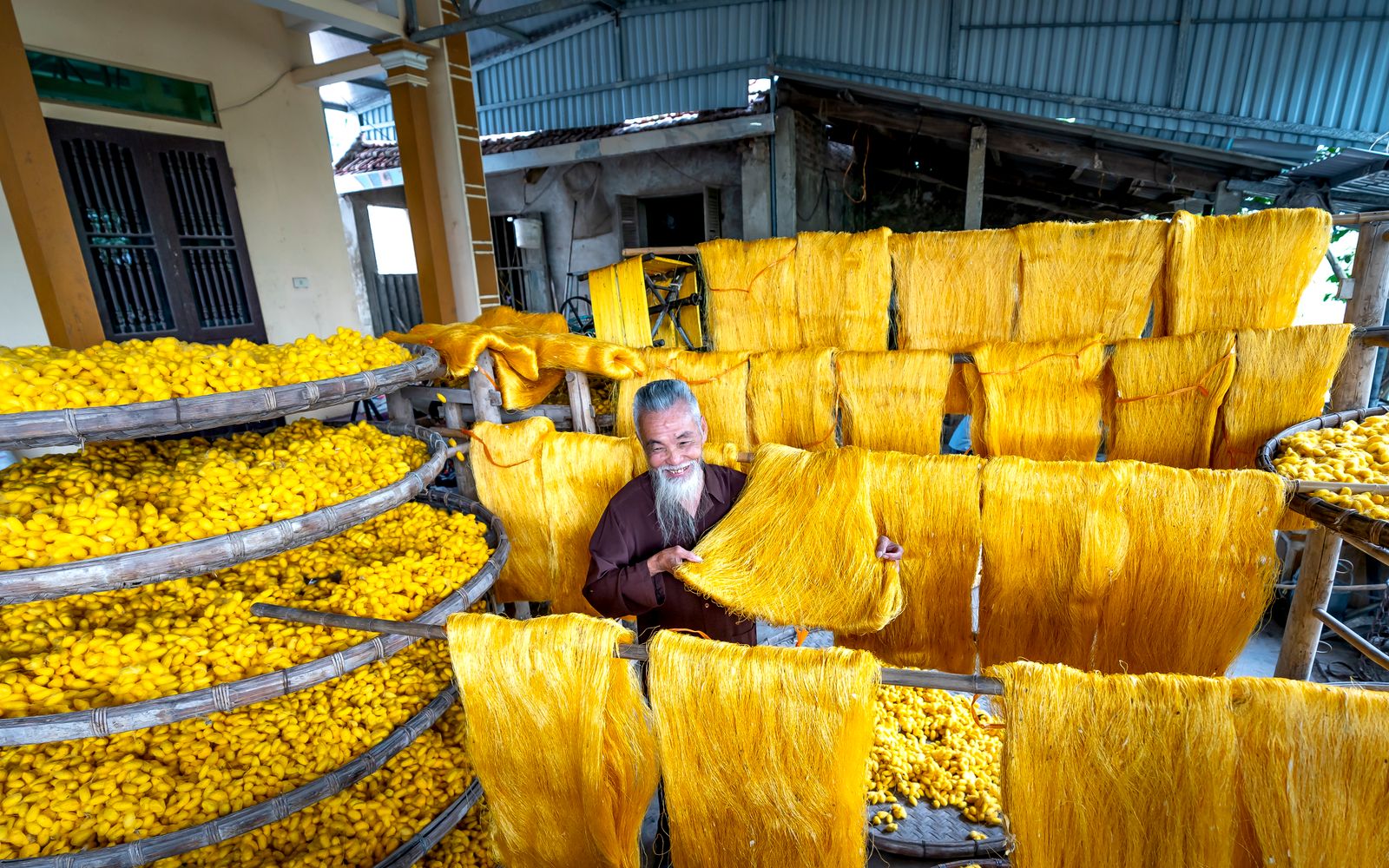 An experienced worker processes yellow silk threads in an indoor production facility.