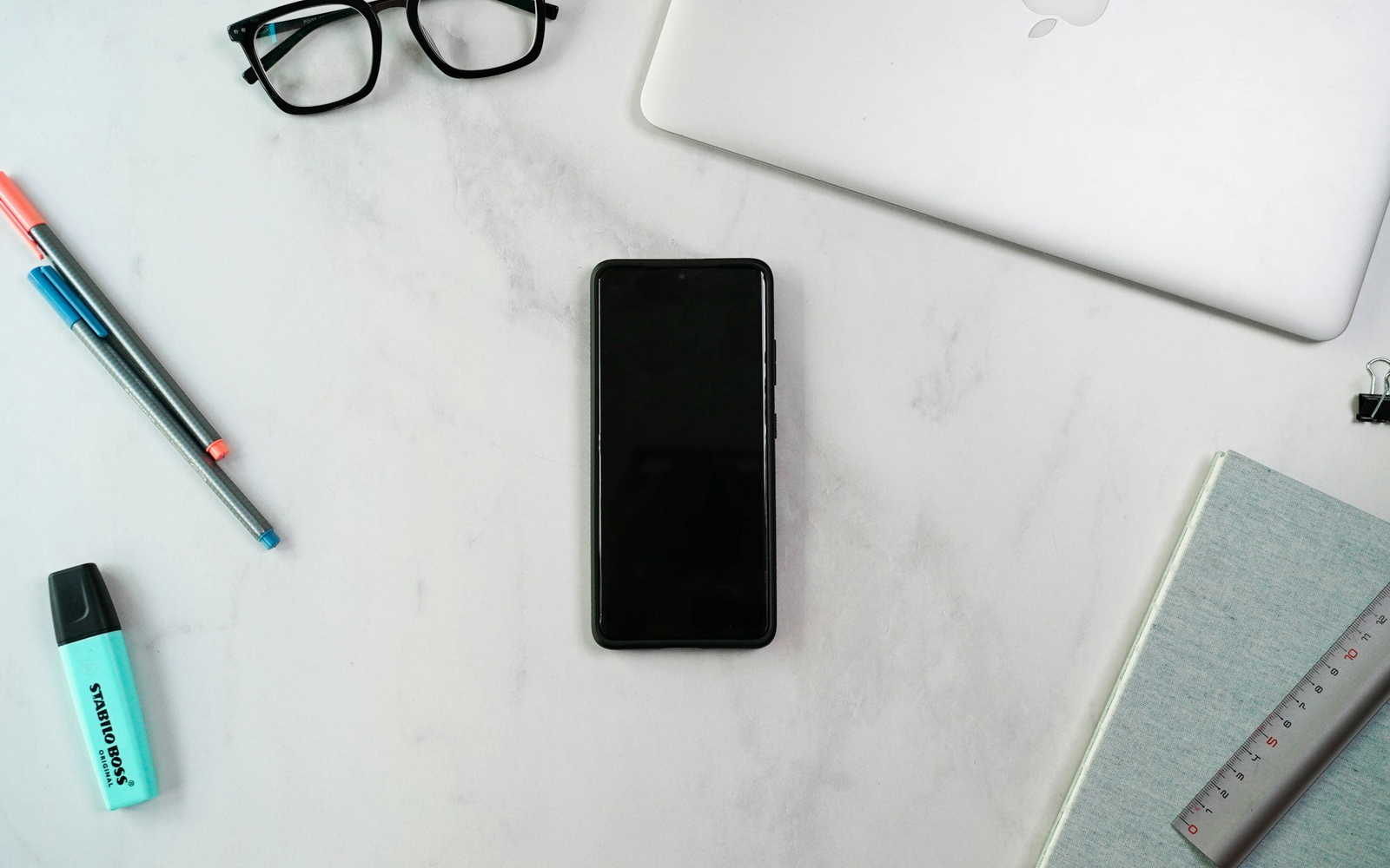Laptop, notebook, glasses, and phone arranged on a developer desk